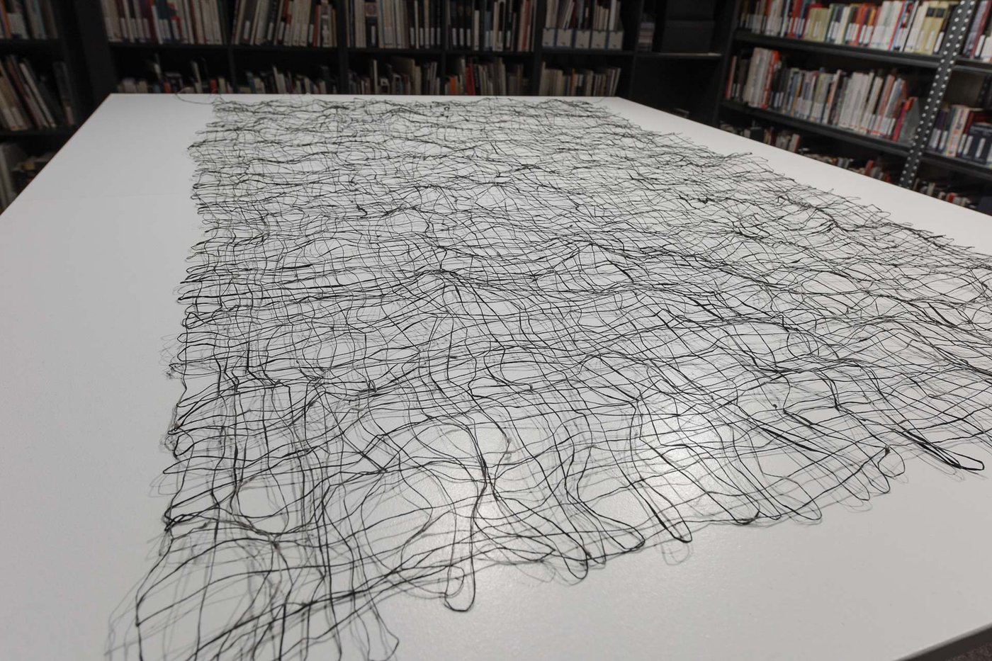 Weißer Tisch auf dem ein Netz aus schwarz-gräulichen Papierfäden liegt.