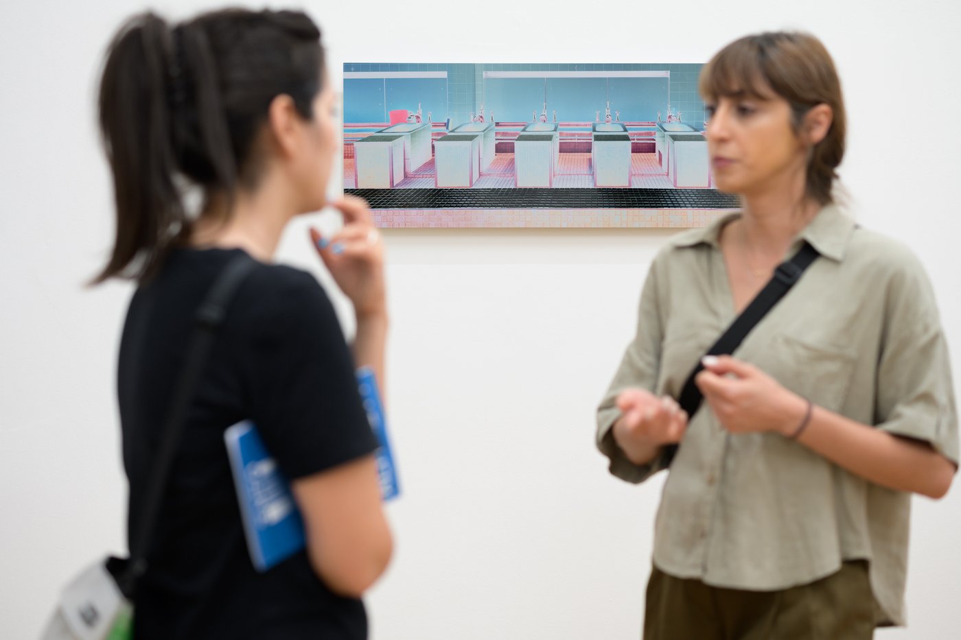 zwei Personen stehen vor einem Kunstwerk und sprechen miteinander, Fokus liegt auf dem rosa Werk an der Wand, Personen im Vordergrund sind unscharf