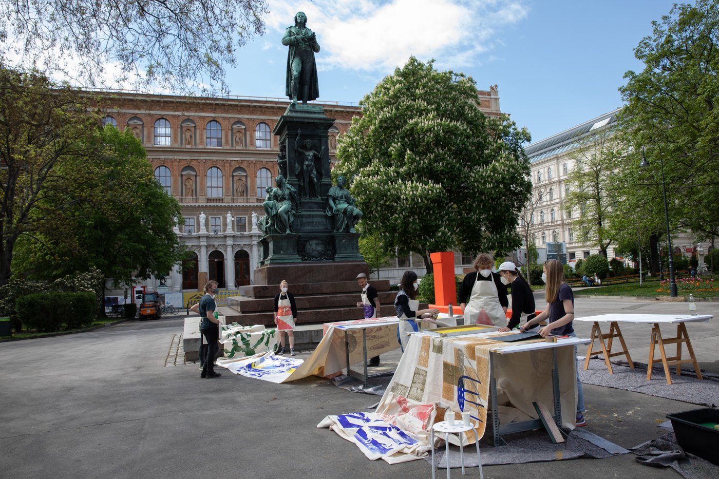 Studierende drucken auf Stoffbahnen vor dem Schillerdenkmal. Im Hintergrund sieht man das Akademiegebäude.