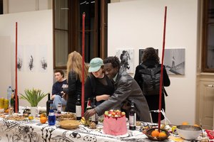 Personen stehen bei einem Tisch der voll mit Essen ist und zeigen auf Dinge