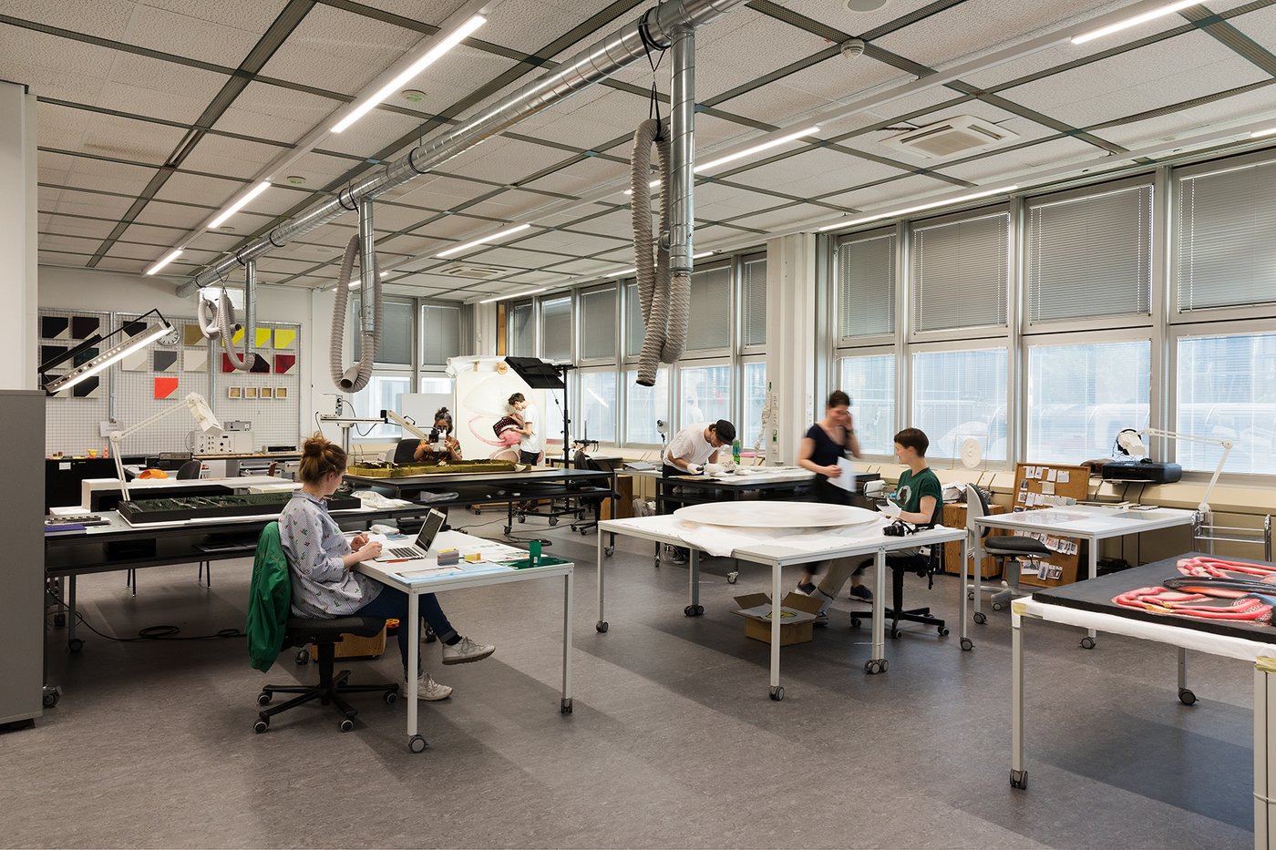 View of a studio room with people sitting at their tables and working on works with technical equipment