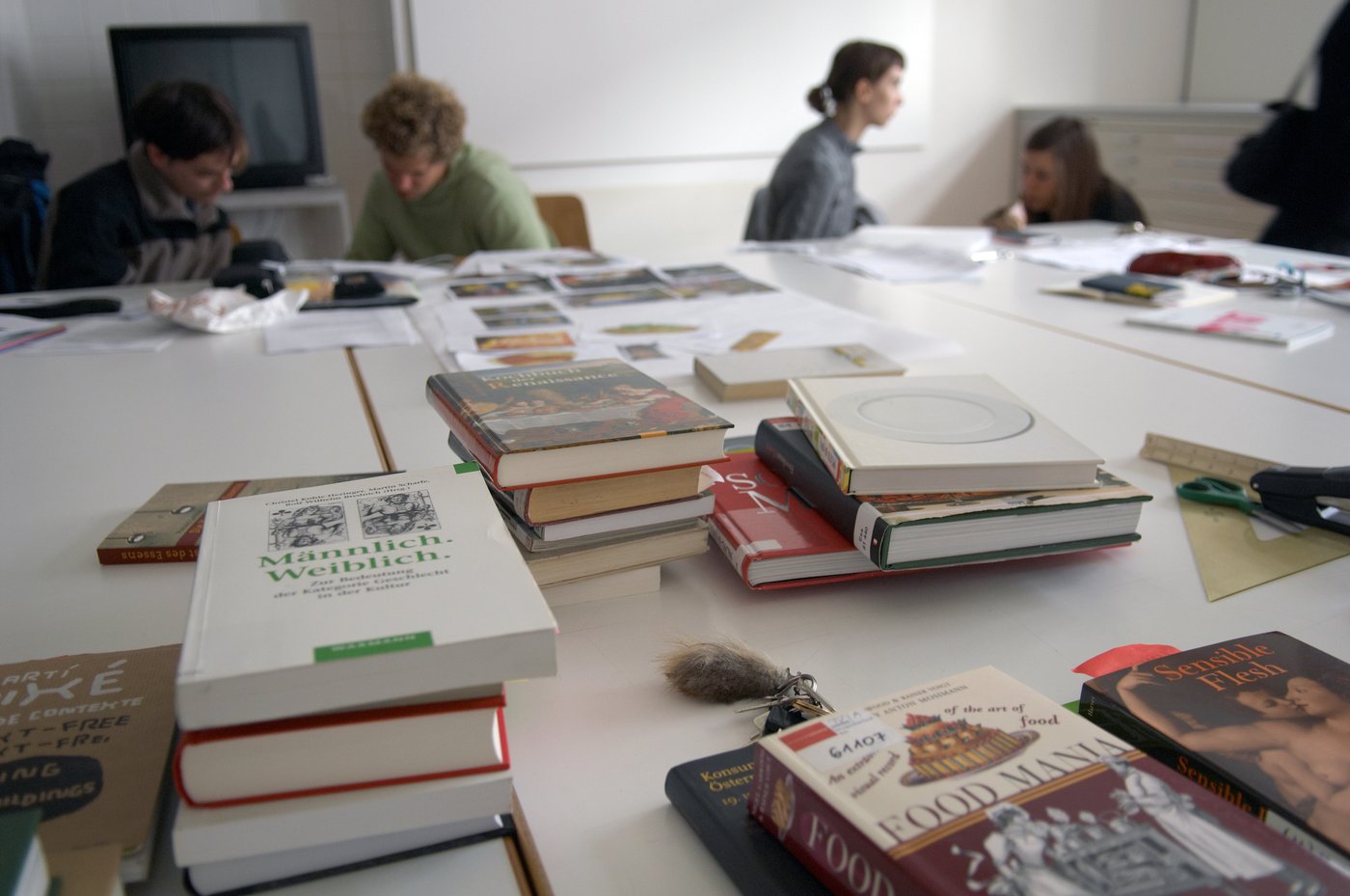 You see students at a table with a lot of stacks of books. They are discussing or bent over work notes.