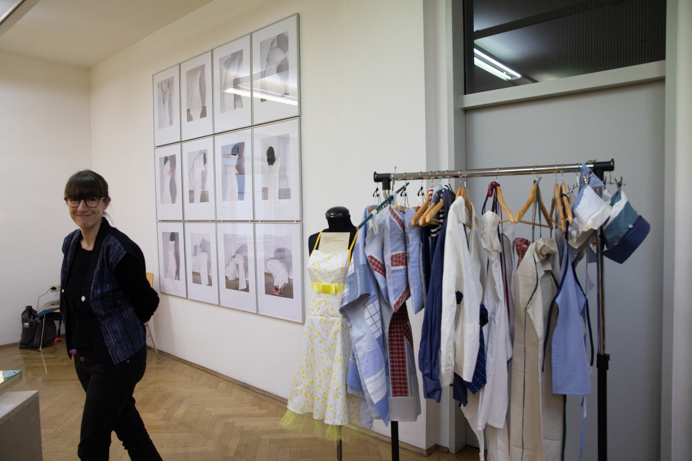 Presentation situation with framed drawings on the wall, a stand with textiles and a visitor.