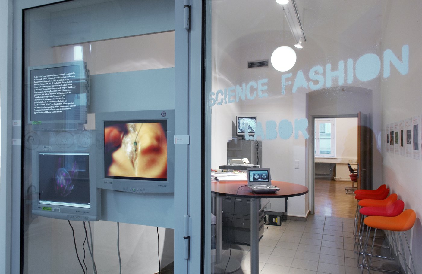 You can see the entrance to the science fashion lab with several monitors, a table and orange armchairs.