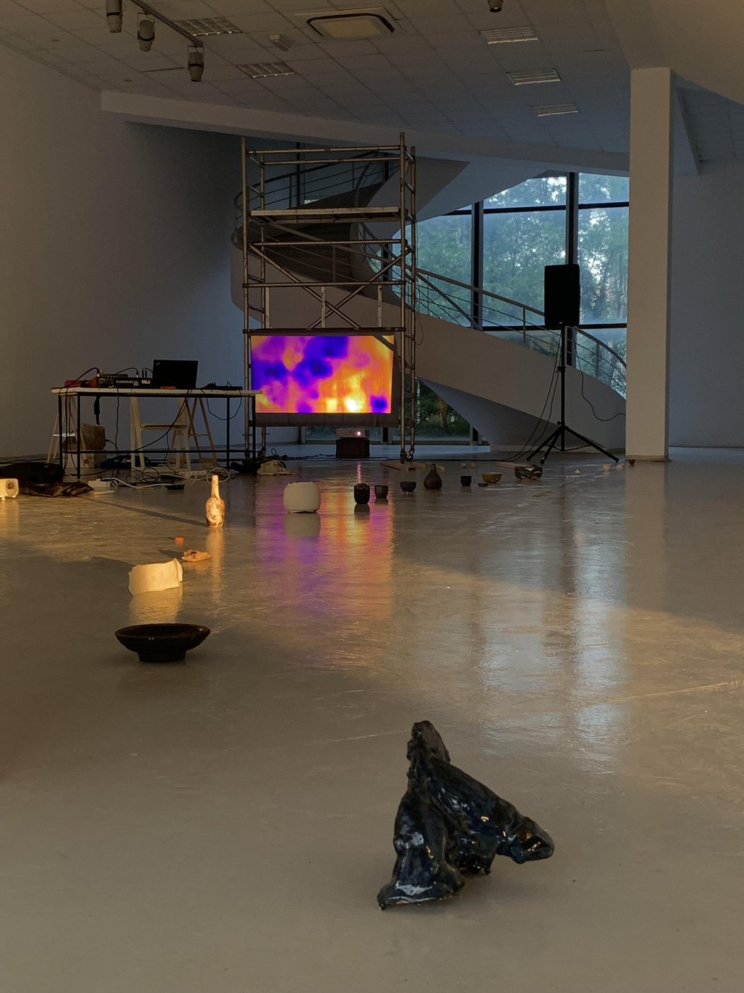 Photo of a showroom with a metal frame on which is a large screen showing a thermal image, in the foreground on the floor small objects lined up.