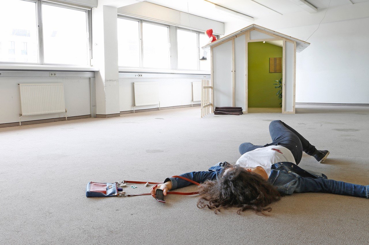 Person on the floor in a room, at the other side a small wooden house with a figure on top