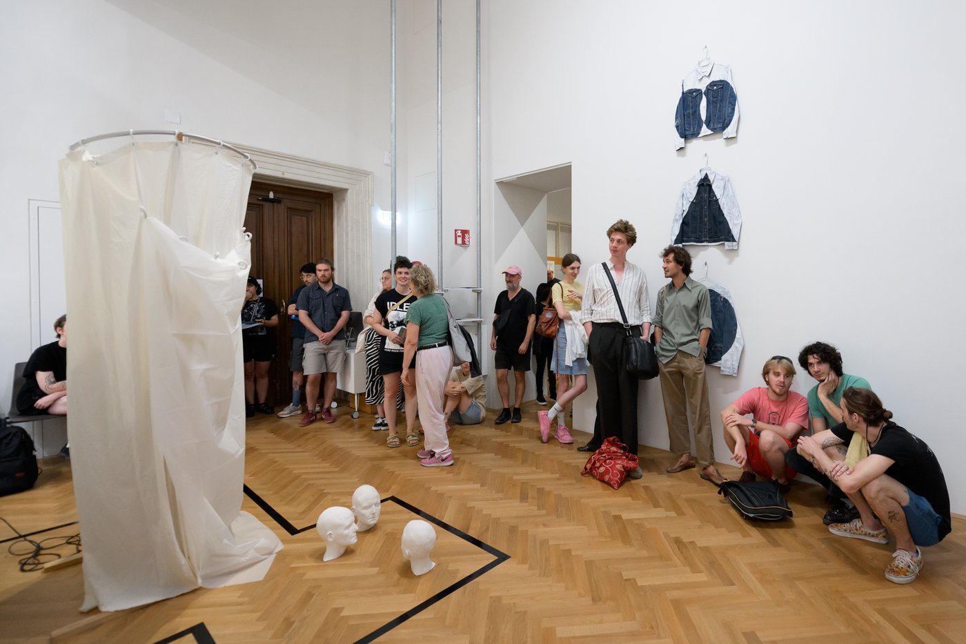 room full of people watching a performance, the artist is hiding in a white shower curtain