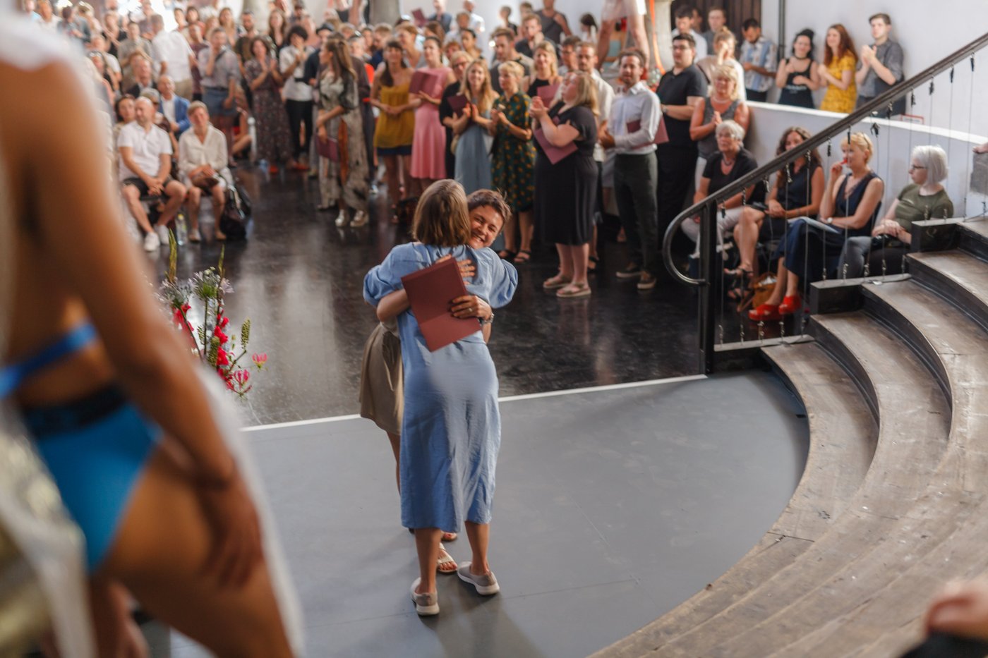 Presentation of certificates during the 2020 graduation ceremony at Prospekthof: a graduand and another woman hug each other joyfully, the other guests in the room applaud.