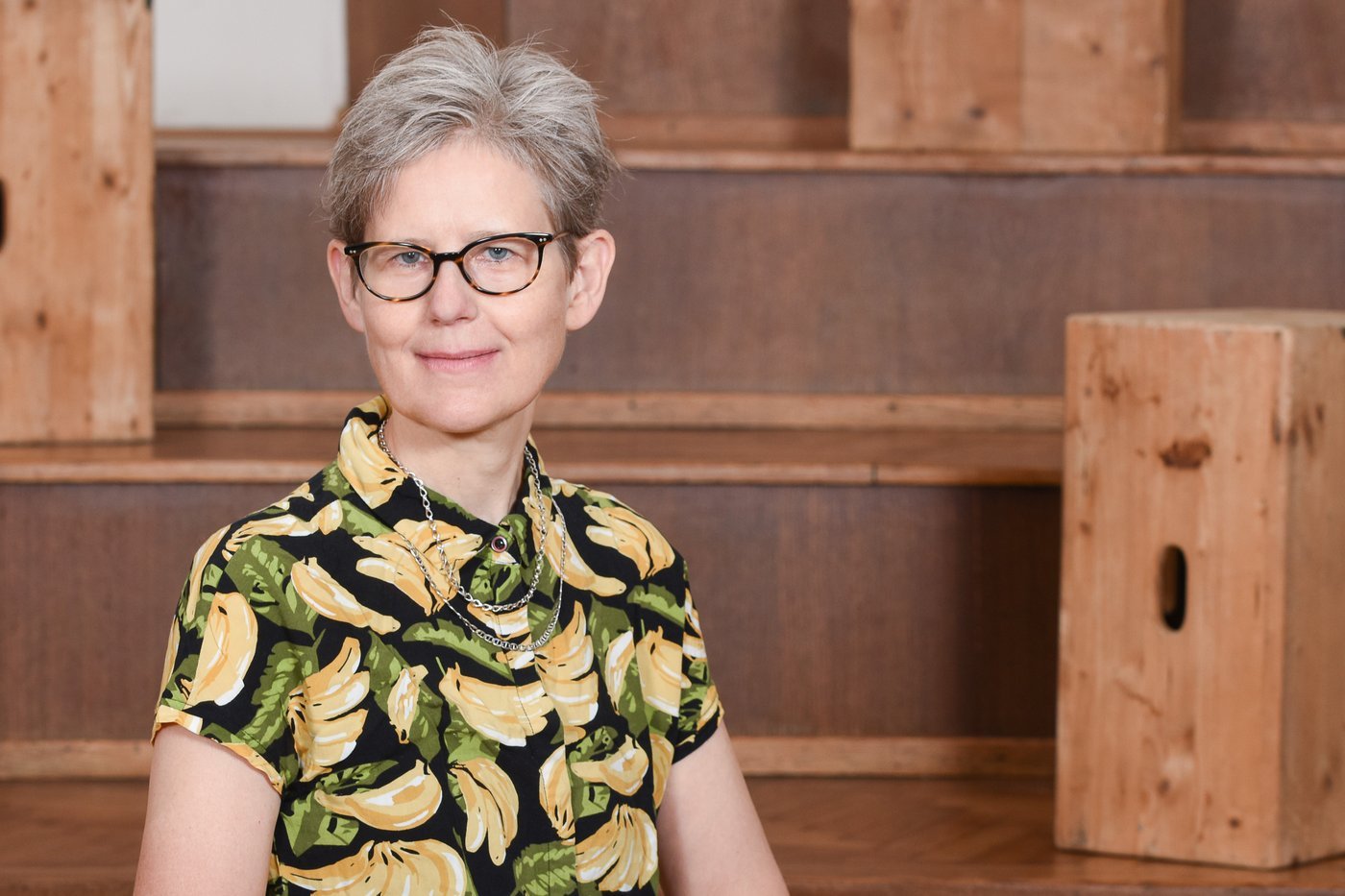 Photo of a woman with white hair and a colorful blouse with banana print smiles at the camera