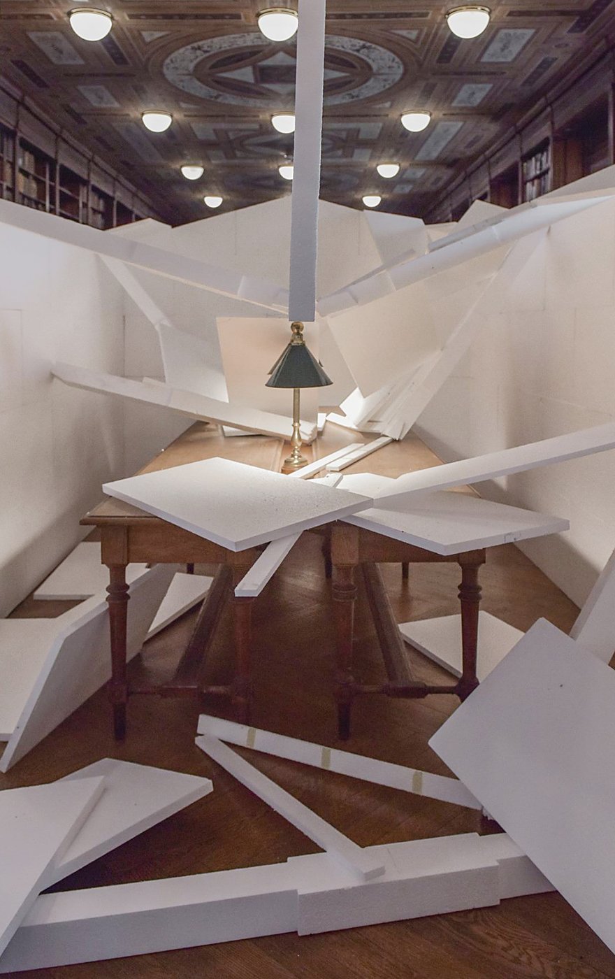 White, collapsing house made of Styrofoam, set up in the reading room of the library.